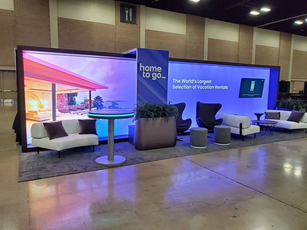 Home to Go 10x20ft backlit trade show display wall with furniture and carpet.